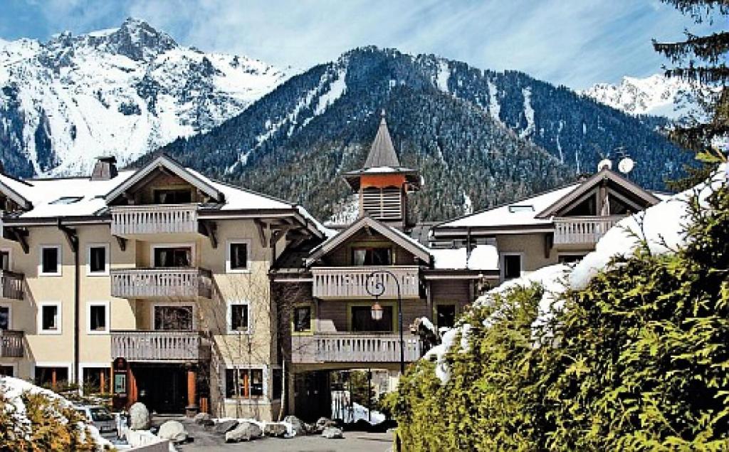 a large building with snow covered mountains in the background at Résidence La Ginabelle - maeva Home - Appartement 4 Pièces 8 Personnes - S 444 in Chamonix