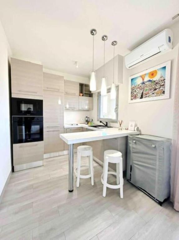 une cuisine avec une table et deux tabourets blancs dans l'établissement Il Gioiello : Apt 2 pers, Clim, Piscine, Parking, à Antibes