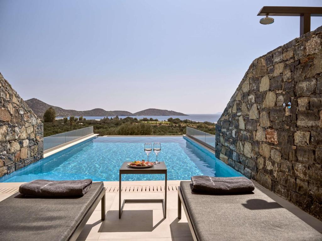 a swimming pool with a table next to a stone wall at Elounda Palm Hotel & Suites in Elounda