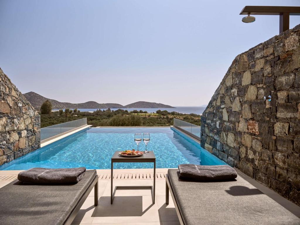 einen Pool mit einem Tisch neben einer Steinmauer in der Unterkunft Elounda Palm Hotel & Suites in Elounda