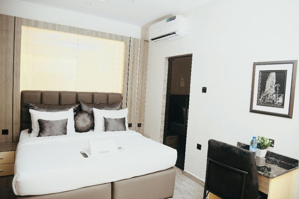 a bedroom with a large white bed and a desk at WosAm Hotels in Ago Iwoye