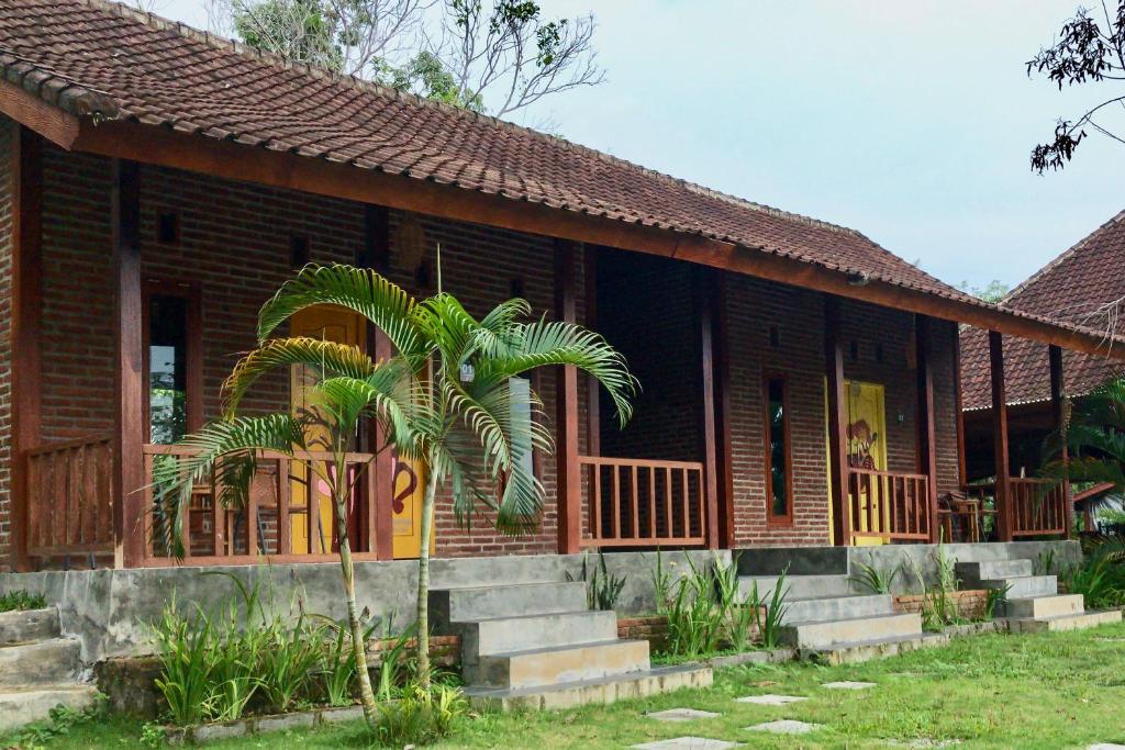 a house with a palm tree in front of it at Kampung Coklat Jembrana Mitra RedDoorz in Jembrana