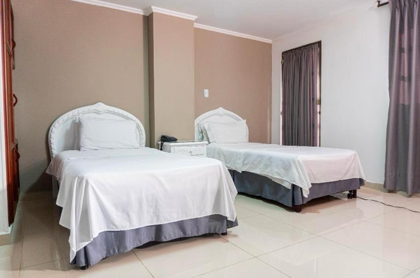 2 camas en una habitación de hotel con sábanas blancas en Hotel Suite Santa Rosa, en Santa Rosa de Cabal