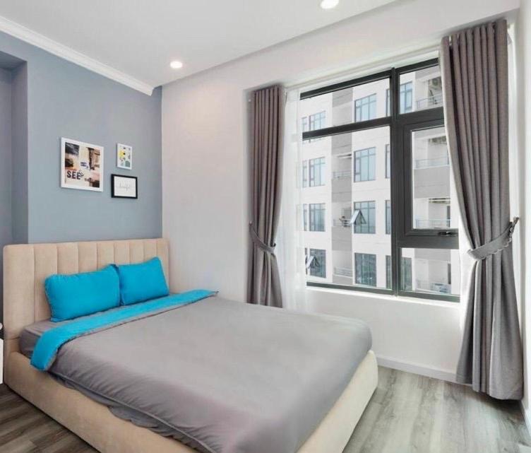 a bedroom with a bed with blue pillows and a window at IMPERIAL PLACE - NATURAL POEM View đẹp - hồ bơi, gym miễn phí in Ho Chi Minh City