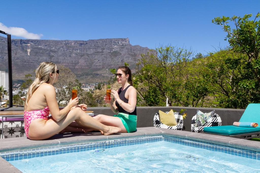 two women sitting next to a swimming pool with drinks at Cape Finest Guest House located in De Waterkant in Cape Town