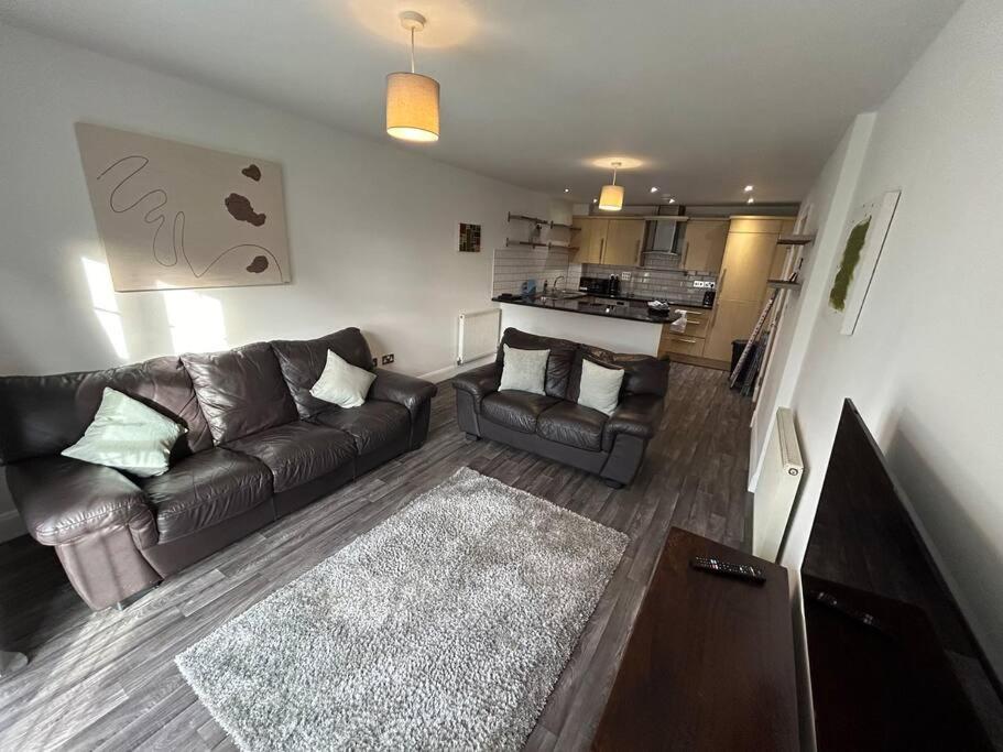 a living room with a leather couch and a kitchen at Spacious 2 Bed 2 Shower Apartment in Crewe