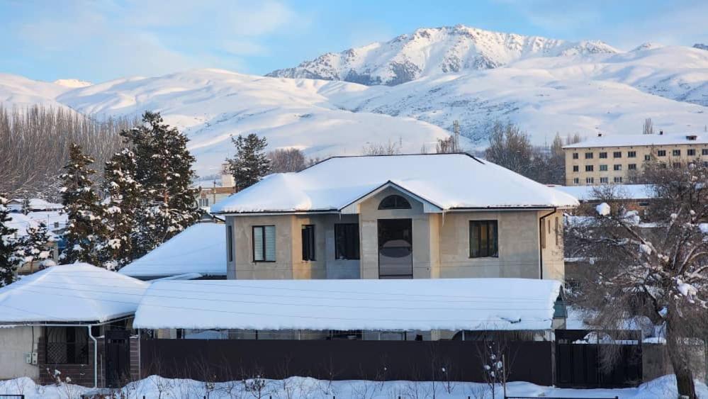 ein schneebedecktes Haus mit Bergen im Hintergrund in der Unterkunft Karakol Yurt Lodge & Homestay in Karakol