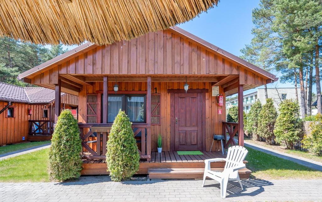 a small wooden cabin with a white chair and a straw roof at Domki Hawana in Dąbki