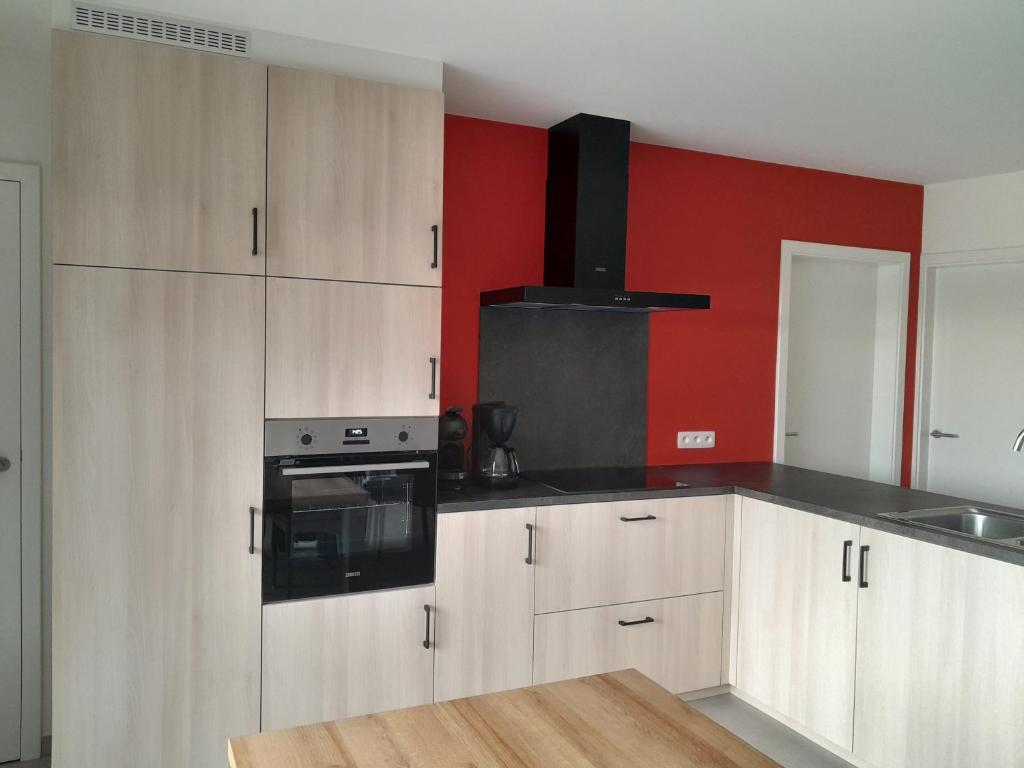 a kitchen with white cabinets and a red wall at Chez Jeannine et Yvo in Mai Cornet