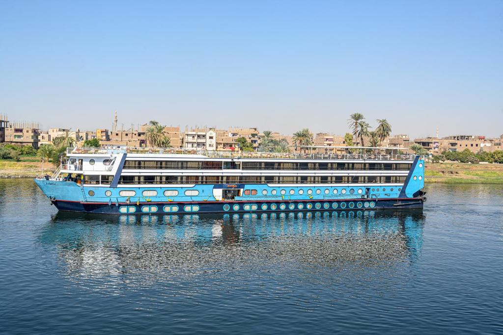 un barco azul en el agua con edificios en el fondo en Magic I Nile Cruise Deluxe Boat The scheduled departure is on Saturday for a 7-day Nile cruise en Luxor