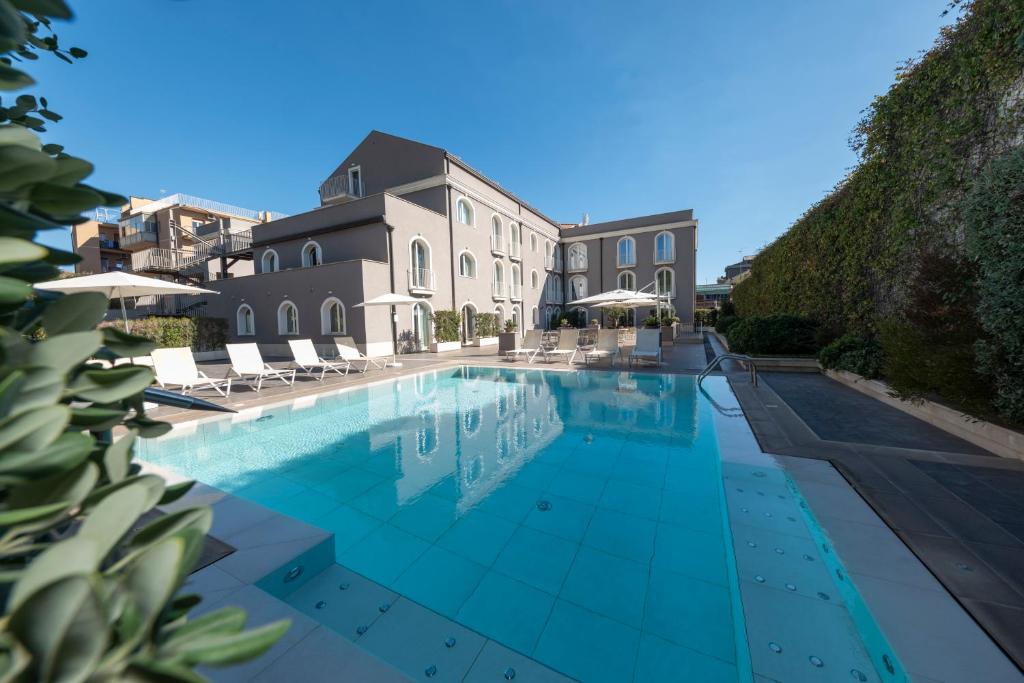 uma piscina com cadeiras e um edifício em Airone City Hotel em Catânia