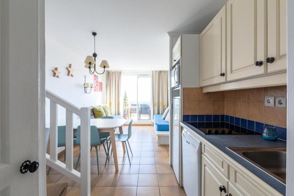 kuchnia z białymi szafkami i stołem z niebieskimi krzesłami w obiekcie Les Appartements aux Restanques du Golfe de St Tropez - maeva Home - Appartement 3 Pièces 6 Personnes - Sélection - vue Mer MAE-6504 w mieście Grimaud