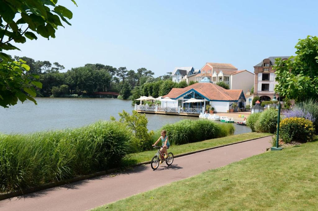 a woman riding a bike down a path next to a river at Résidence Port Bourgenay - maeva Home - Appartement 3 Pièces 7 Personnes - 714 in Talmont