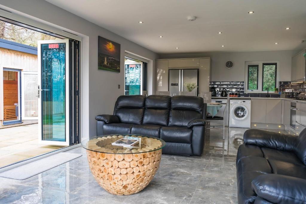 a living room with black leather furniture and a kitchen at Pure relaxation at it's finest, offering moments of harmony and tranquillity - Sauna & Hot tub in Shanklin