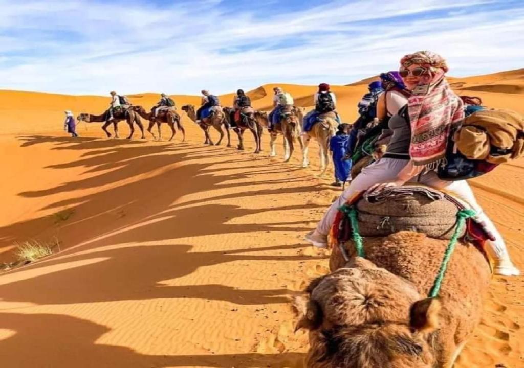 Eine Gruppe von Menschen, die auf Kamelen in der Wüste reiten in der Unterkunft Desert Season Camp in Merzouga