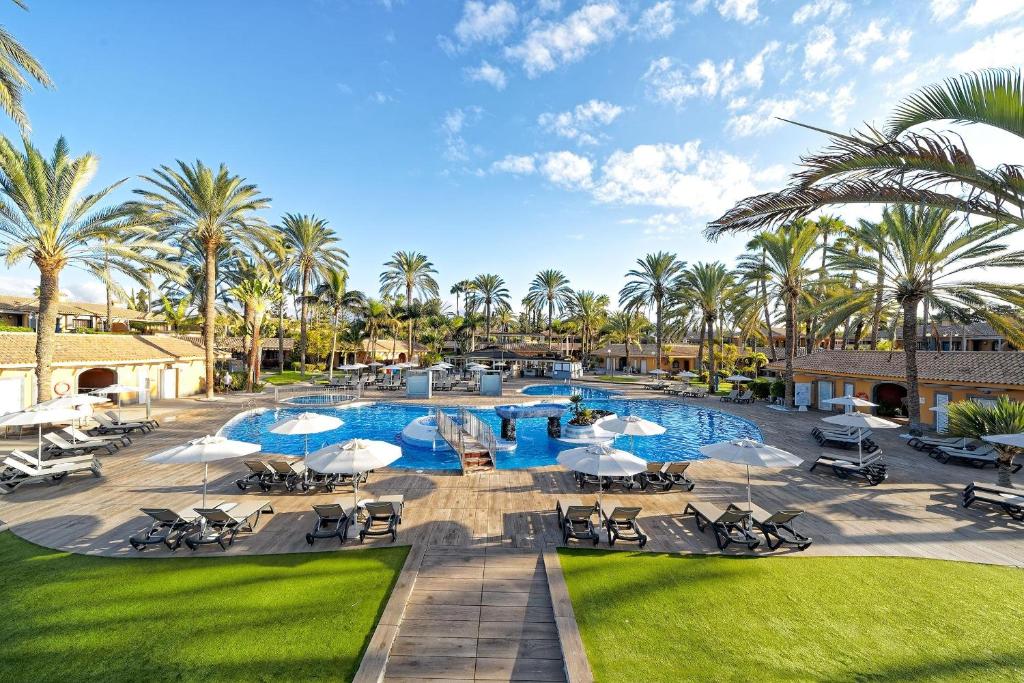 ein Resortpool mit Liegestühlen, Sonnenschirmen und Palmen in der Unterkunft Suites & Villas by Dunas in Maspalomas