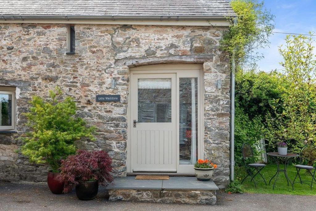 uma casa de pedra com uma porta branca e plantas em Luxury self-contained cottage for two with hot tub em Staverton