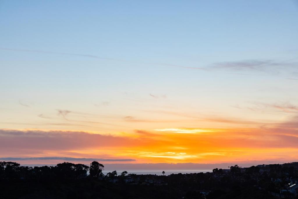 a sunset in the sky with trees in the foreground at 'Sunsets Over Catalina' - An Insider's Secret Hideaway with an Ocean View! in Dana Point