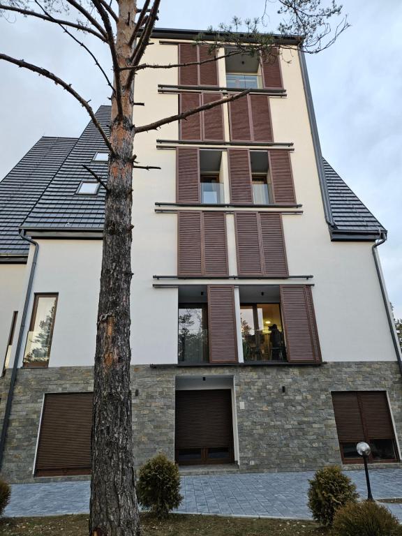 a tall building with brown shuttered windows and a tree at Studio Apartman Nomad Divčibare in Divčibare