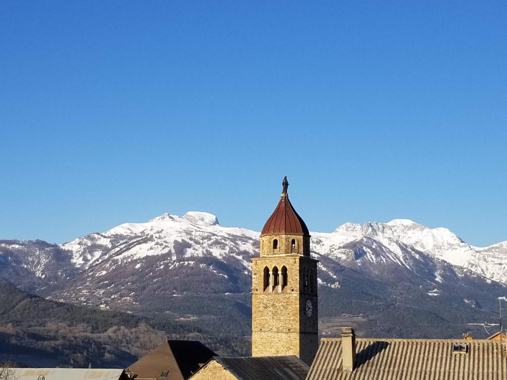 uma torre do relógio com montanhas cobertas de neve ao fundo em Grande maison familiale en Ubaye em Faucon-de-Barcelonnette