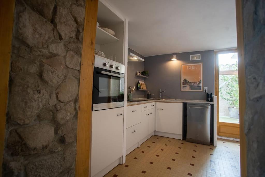 a kitchen with white cabinets and a stone wall at Lovely house with courtyard and terrace near canal du Midi in Trèbes