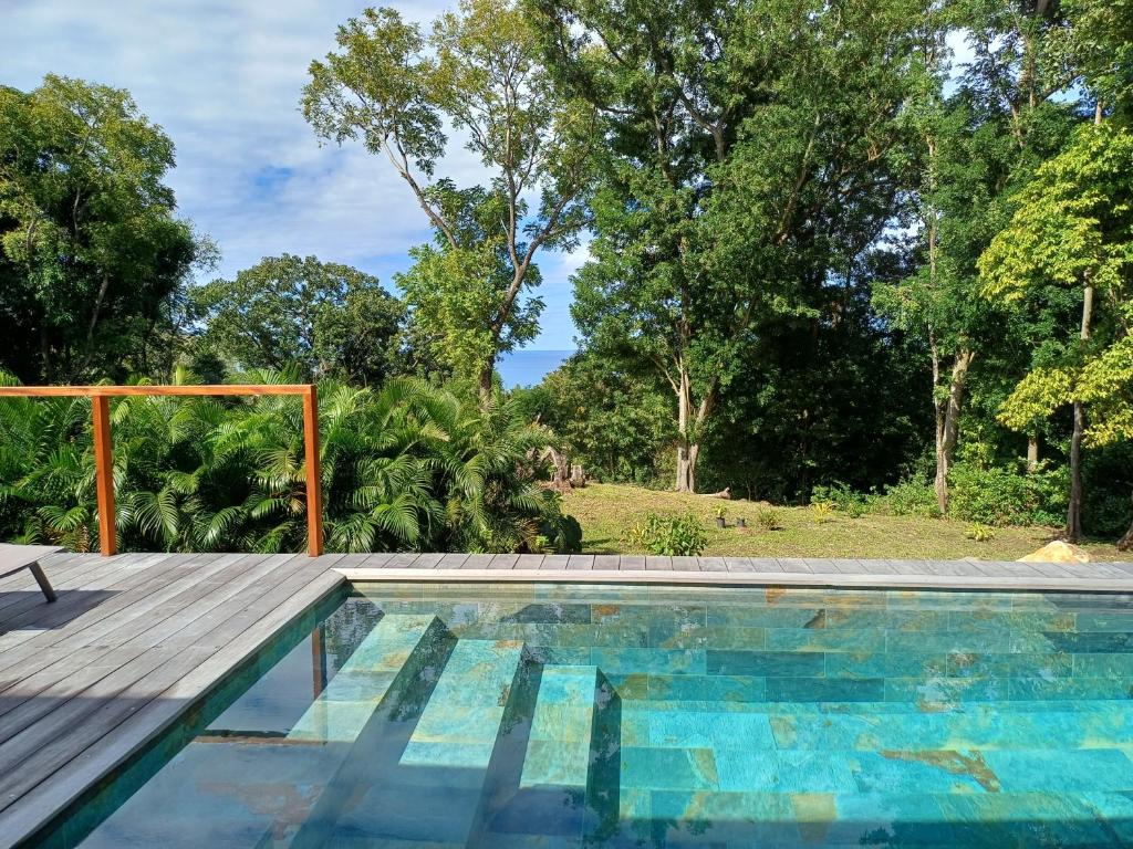 una piscina al aire libre con una terraza de madera y árboles en Lodge belle nature, piscine privée, grand jardin, 900 m de la plage de grande anse, en Deshaies