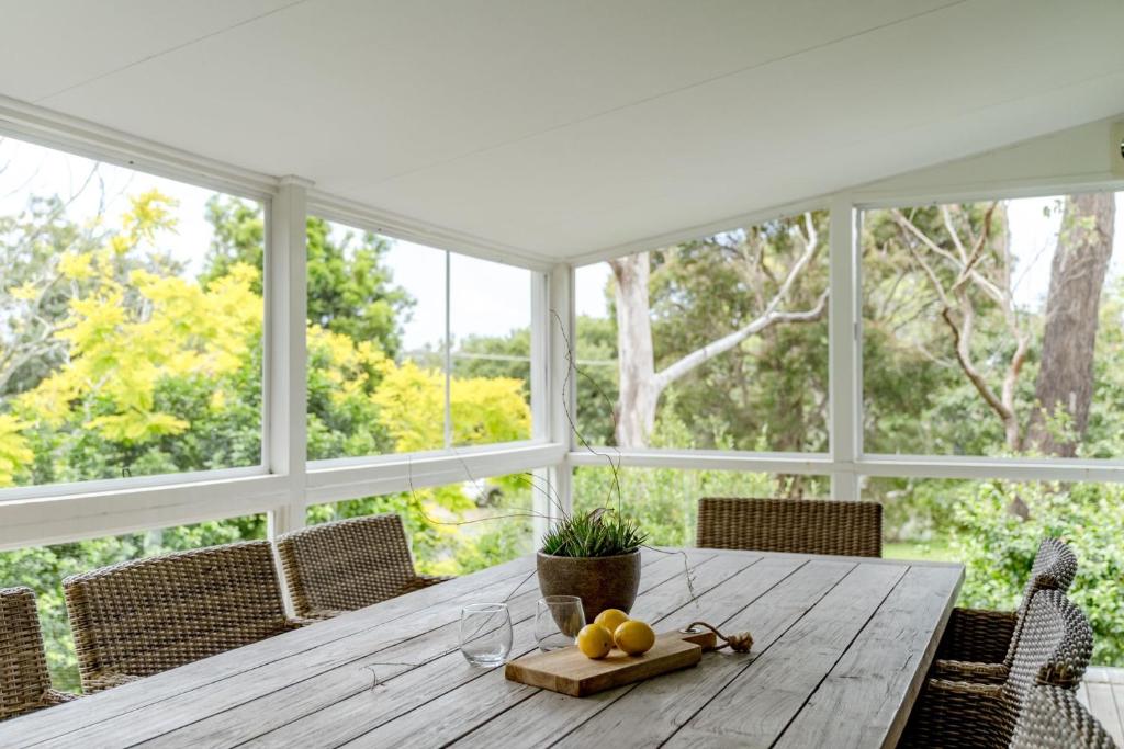 a dining room with a wooden table and windows at Narrawallee Beach House in Narrawallee
