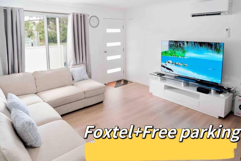 uma sala de estar com um sofá branco e uma televisão de ecrã plano em Fully renovated 3 bedroom house & Free Parking em Gold Coast
