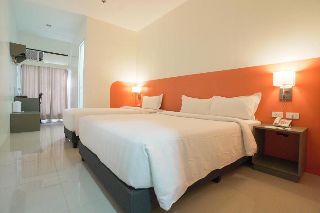 a hotel room with two beds and an orange wall at Travelbee Airport Inn in Mactan