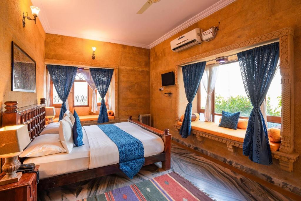 a bedroom with a bed with blue curtains and windows at Hotel Royal Lakhina Jaisalmer in Jaisalmer