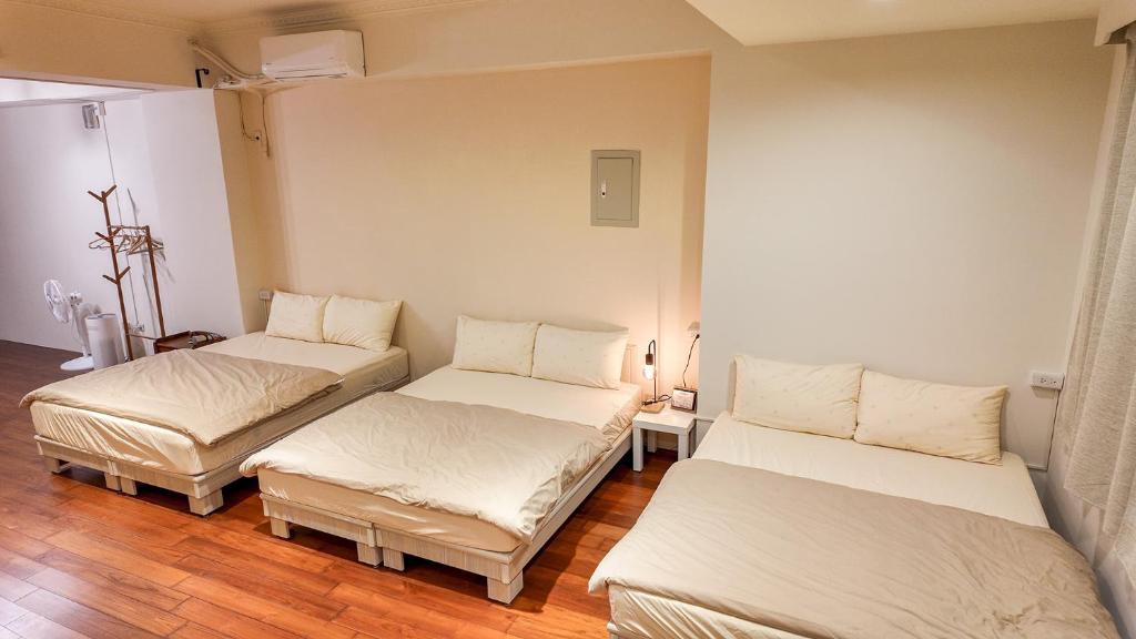 um quarto com 3 camas num quarto com pisos de madeira em Maybe Homestay em Longjing