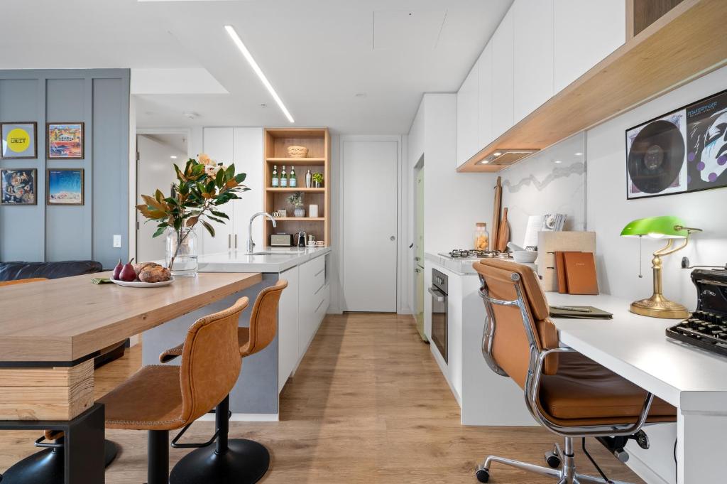 cocina con armarios blancos, escritorio y sillas en Brisbane Luxury Gabba Apartment en Brisbane