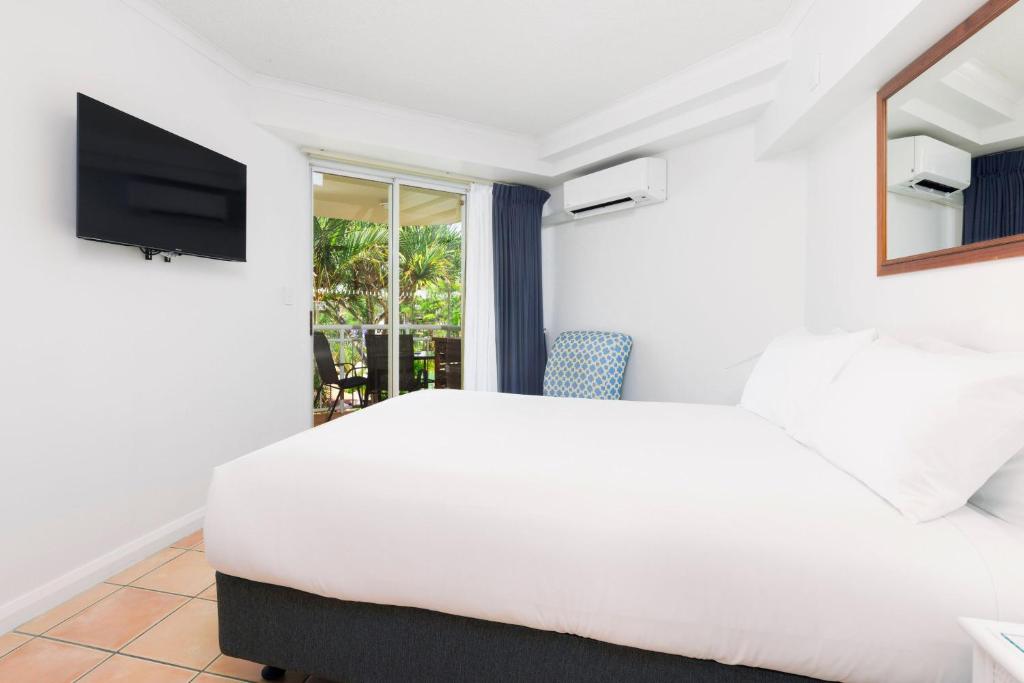um quarto com uma cama branca e uma televisão em BreakFree Alexandra Beach em Alexandra Headland