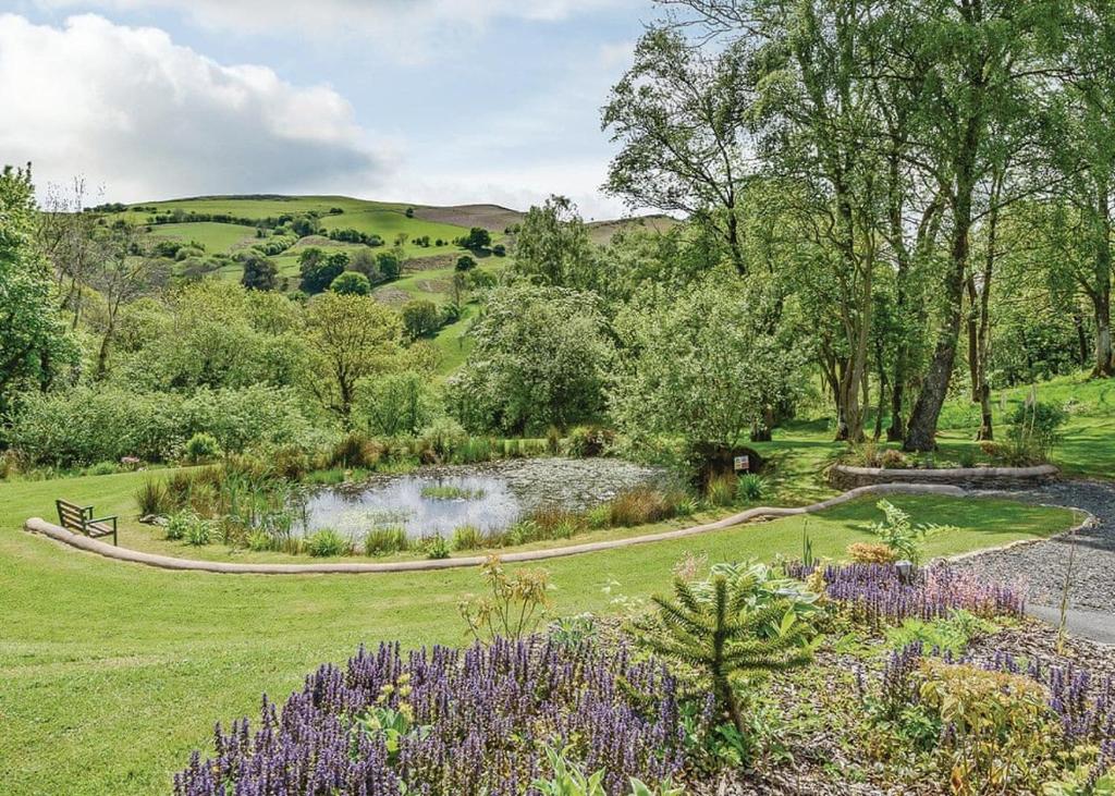 a garden with a pond and flowers in a field at Slate House Lodges in Llandinam
