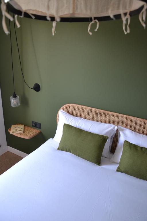 a bedroom with a white bed with two green pillows at Hôtel La Garrigue & Bar Piscine in Venasque