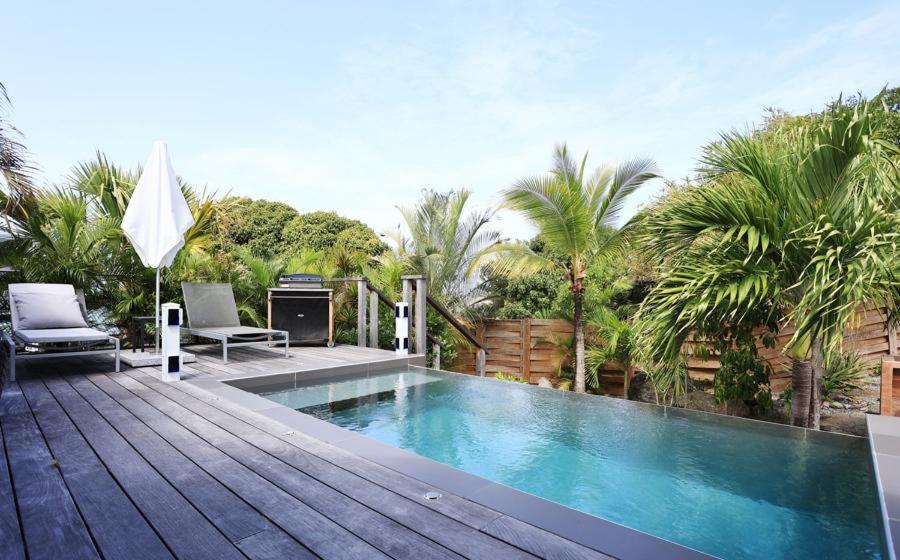 a swimming pool on a wooden deck with chairs and palm trees at Luxury Vacation Villa 14 in Anse des Cayes
