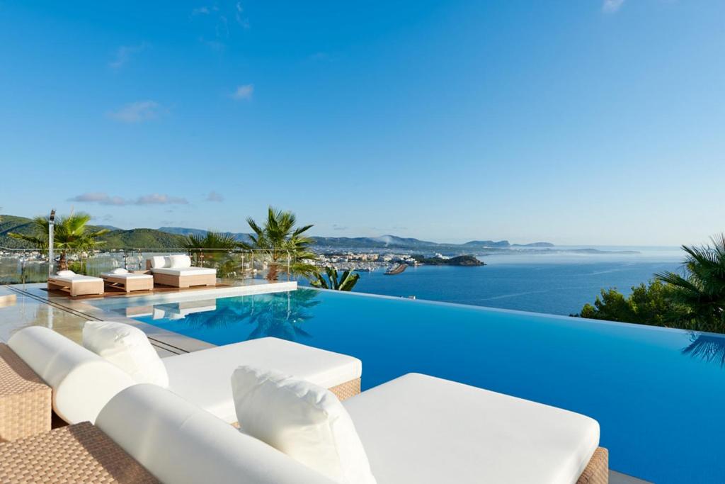 a pool with white chairs and the ocean at Casa Minnustras - Santa Eulalia in Santa Eularia des Riu
