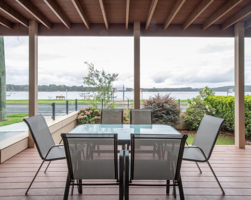 a patio with a glass table and chairs on a deck at Premium Views from Spacious Beachside Home in Batemans Bay