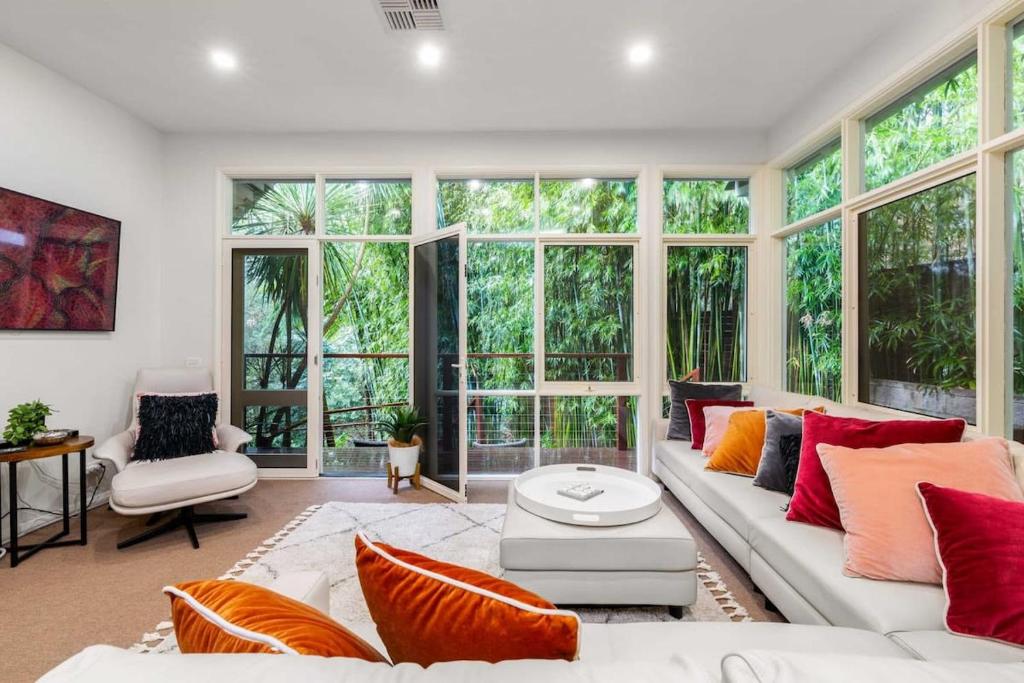 sala de estar con sofá blanco y ventanas grandes en Leafy Retreat with Deck & City Convenience, en Sídney