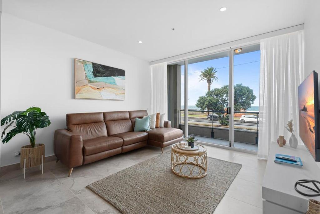 sala de estar con sofá marrón y ventana grande en Bespoke 2-Bed Beachfront Apartment, en Melbourne