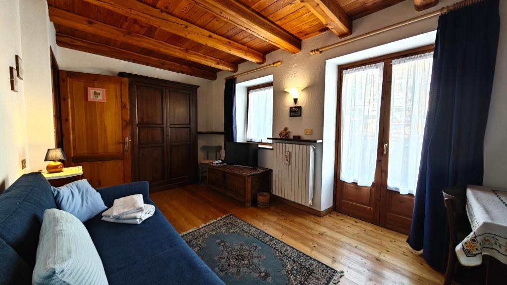 una sala de estar con sofá azul y techos de madera. en Hostdomus - La Posta apartment, en Pragelato