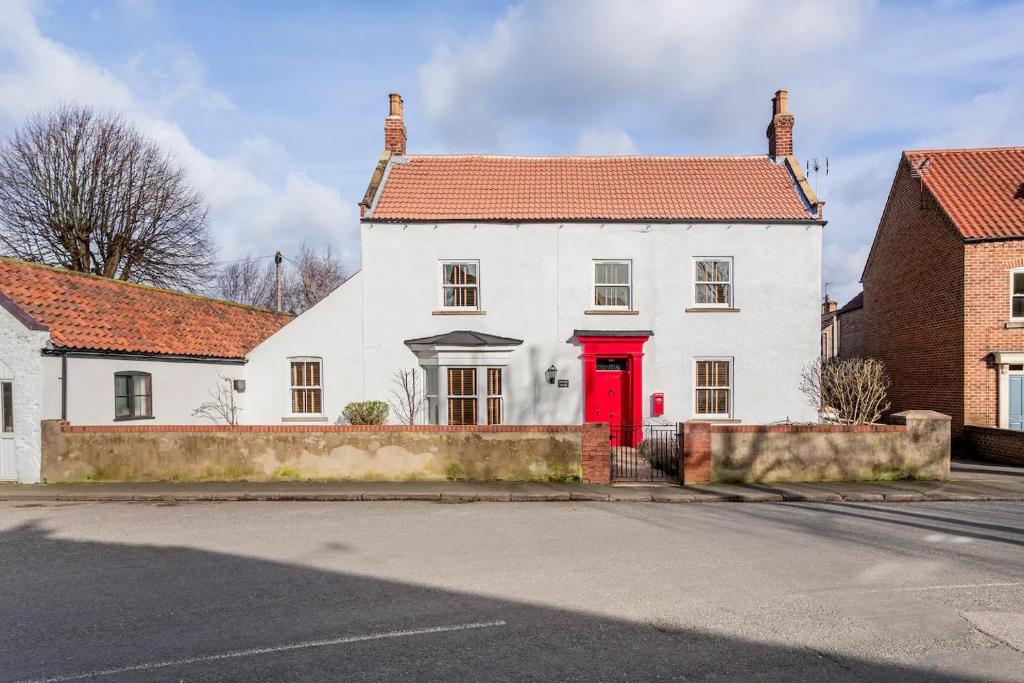 a white house with a red door on a street at Pinfold House in Wistow