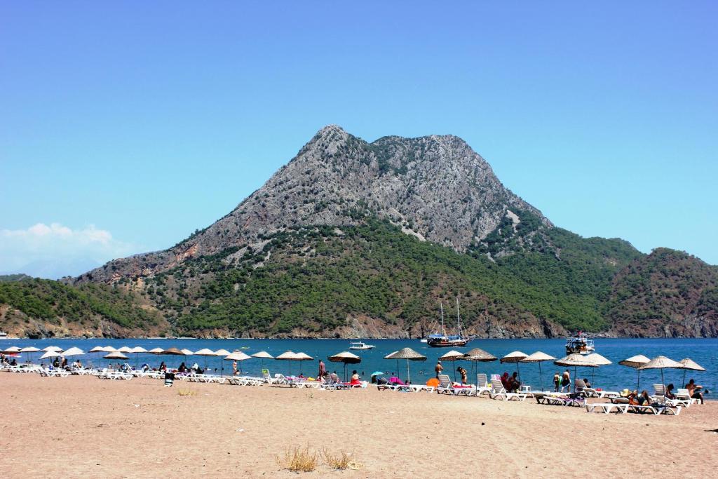 a beach with chairs and umbrellas and a mountain at Adrasan Shambala Hotel in Adrasan