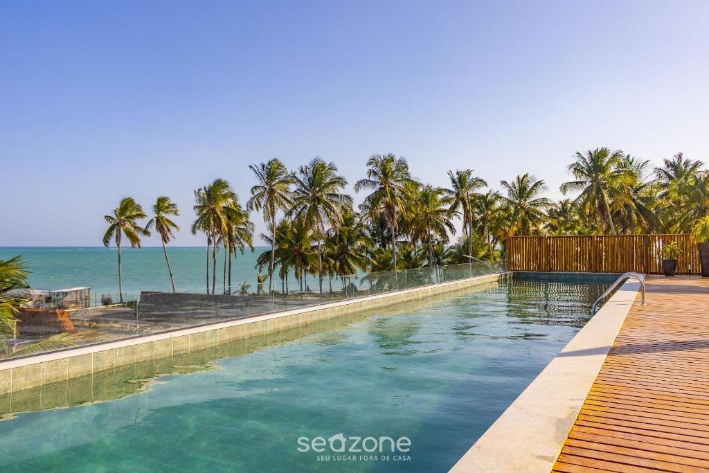 - une piscine avec des palmiers et l'océan dans l'établissement Belo apto a 50m da praia de Tatuamanha TMHC104, à Tatuamunha