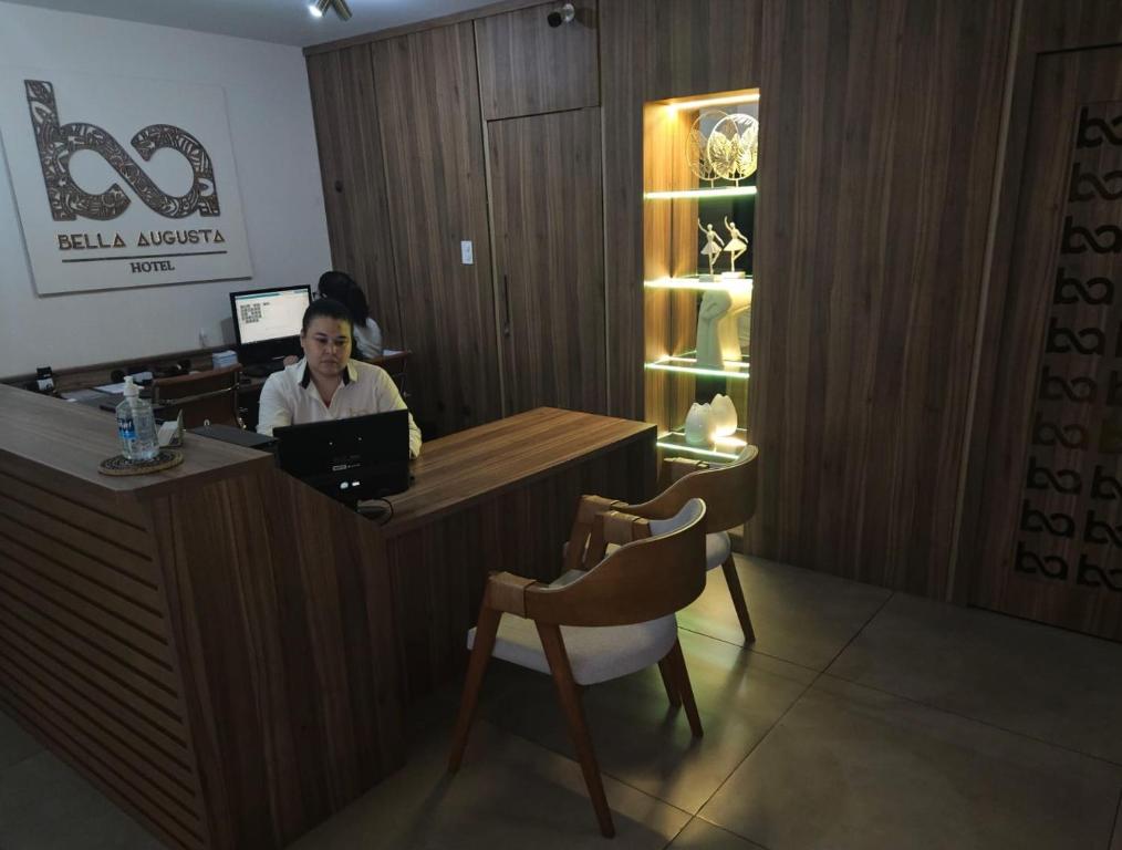 a woman sitting at a reception desk with a laptop at Bella Augusta Hotel in São Paulo