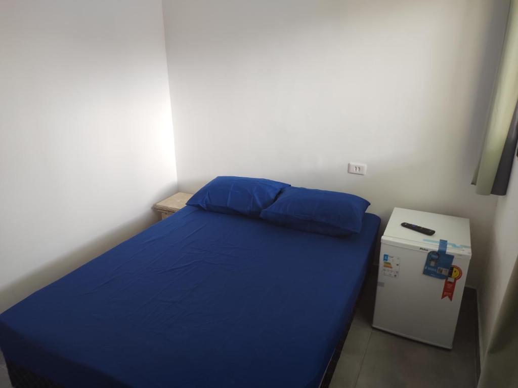 Habitación pequeña con cama azul y nevera pequeña. en Casa Cardoso en Bertioga