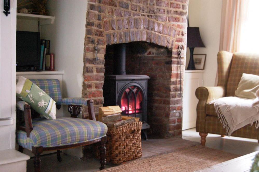 The Old Smoke House في Kent: غرفة معيشة بها موقد مع كراسي وأريكة