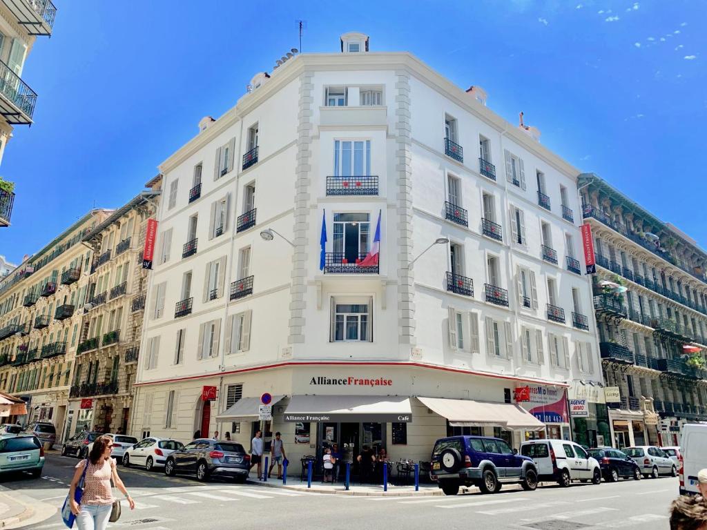 un edificio blanco alto en una calle de la ciudad con coches en Résidence de l'Alliance, en Niza