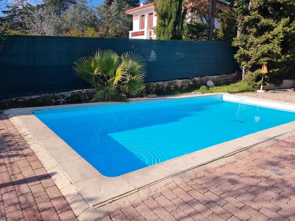 a blue swimming pool in a yard with a fence at Les Palmiers in Nice