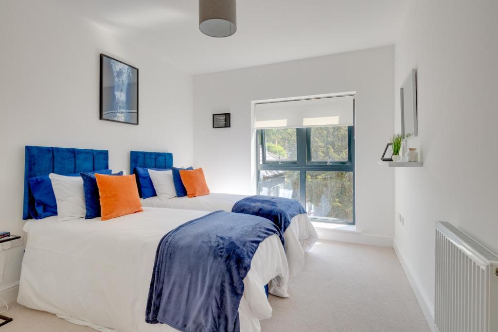 2 bedden in een witte kamer met blauwe en oranje kussens bij Stevenage Luxury 1 Bed Apartment Sleeps 4 WIFI Free Parking Secure by JM Short Lets in Stevenage